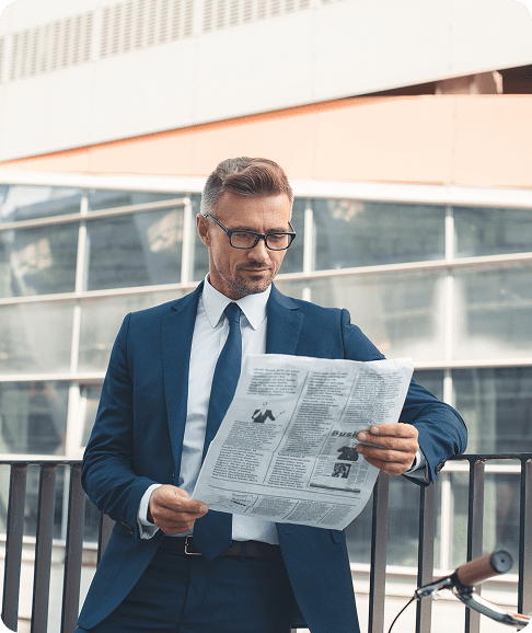 Man in suit reading newspaper outdoors.